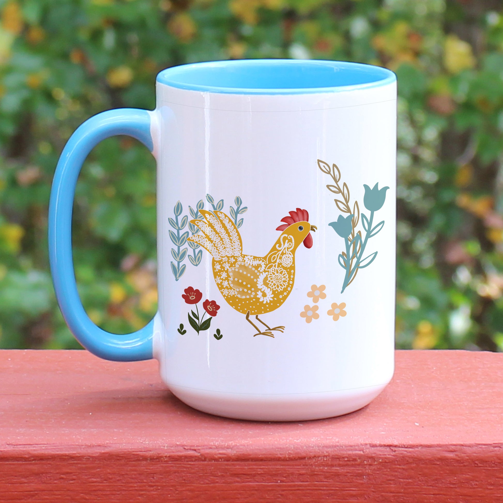 Chicken and rooster themed blue handle ceramic mug with floral designs in blue, yellow, and red.