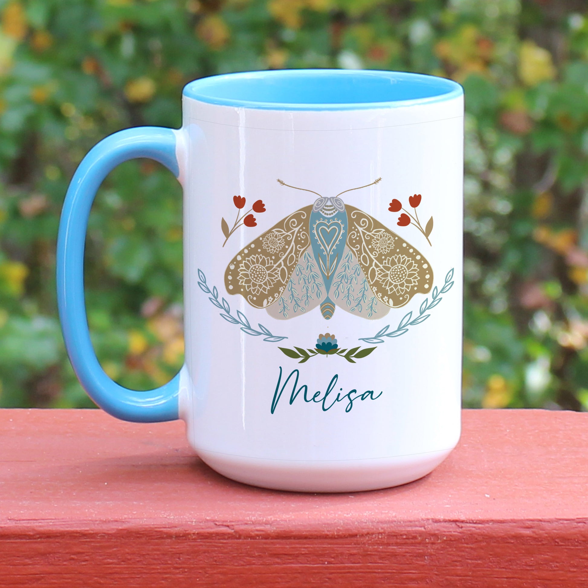 Boho floral moth mug personalized with name. The mug has a blue handle.