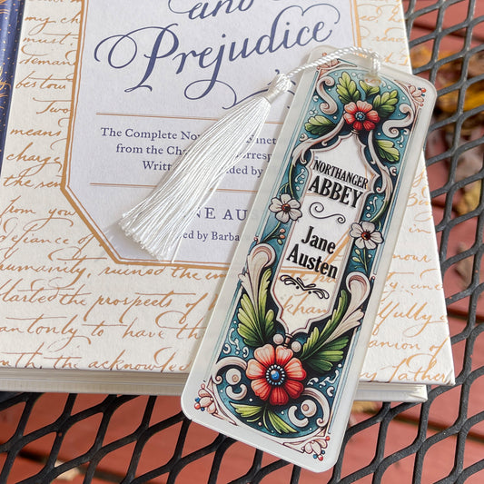 Jane Austen Northanger Abbey floral acrylic bookmark with tassel laying on closed Pride and Prejudice book.