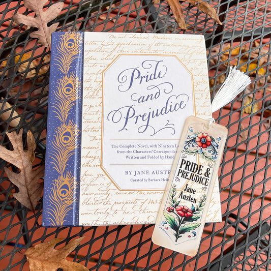 Jane Austen Pride and Prejudice floral acrylic bookmark with tassel laying on closed Pride and Prejudice book.