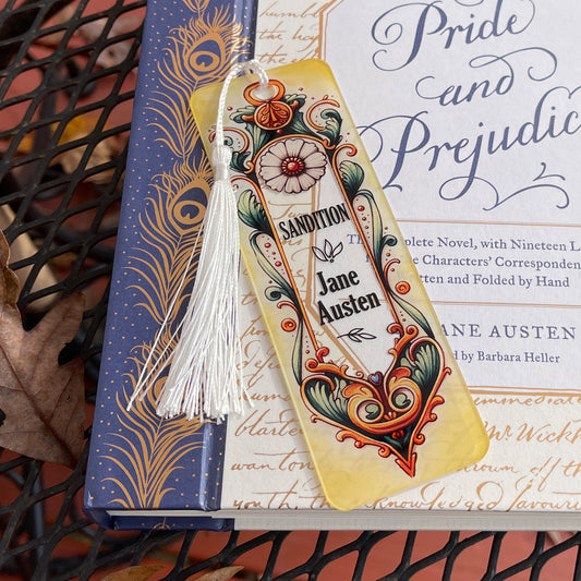 Jane Austen Sandition floral acrylic bookmark with tassel laying on closed Pride and Prejudice book.