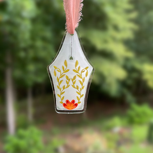 Acrylic fountain pen nib ornament featuring garden flower design hanging against a blurred background.