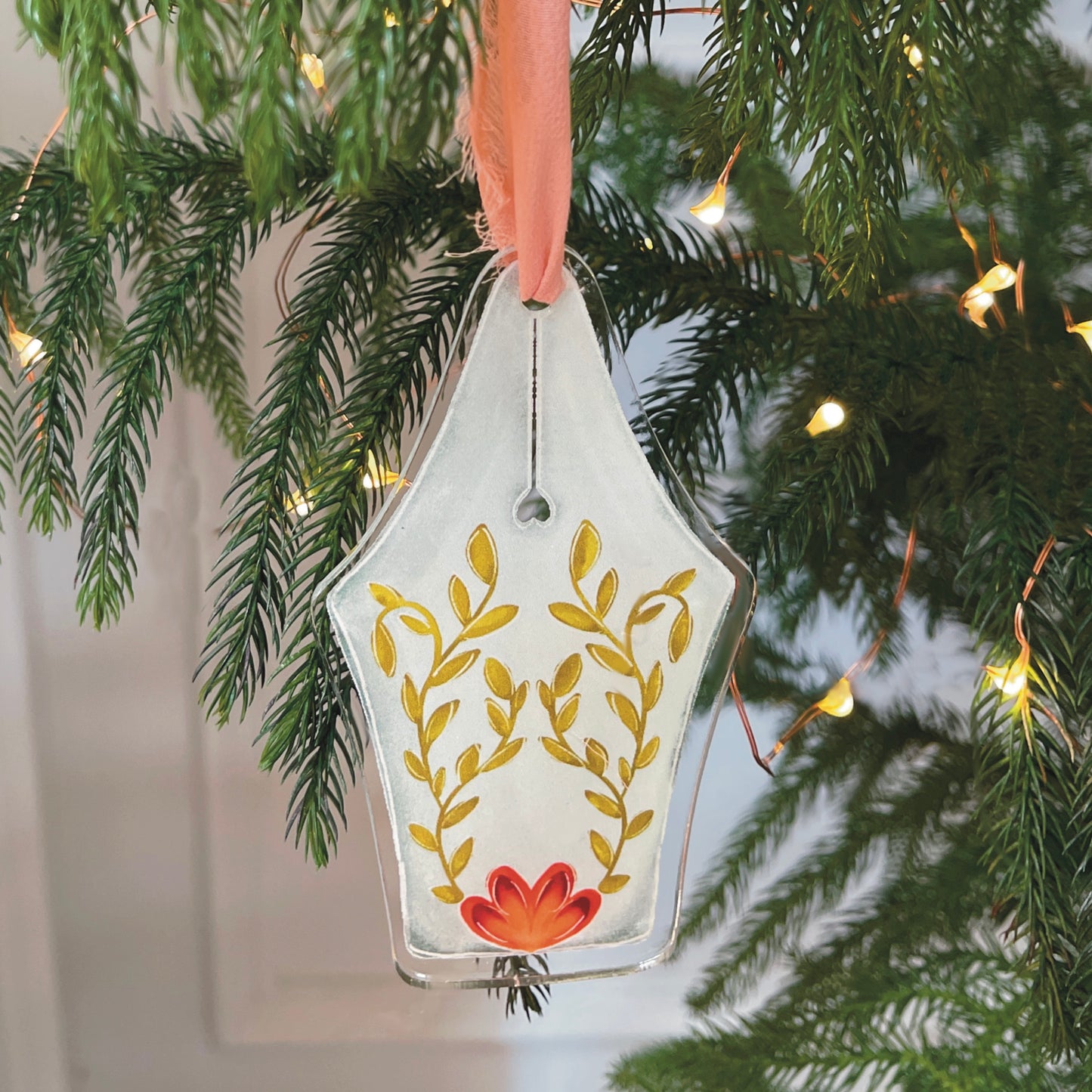 Acrylic fountain pen nib ornament featuring garden flower design hanging on a Christmas tree with lights.