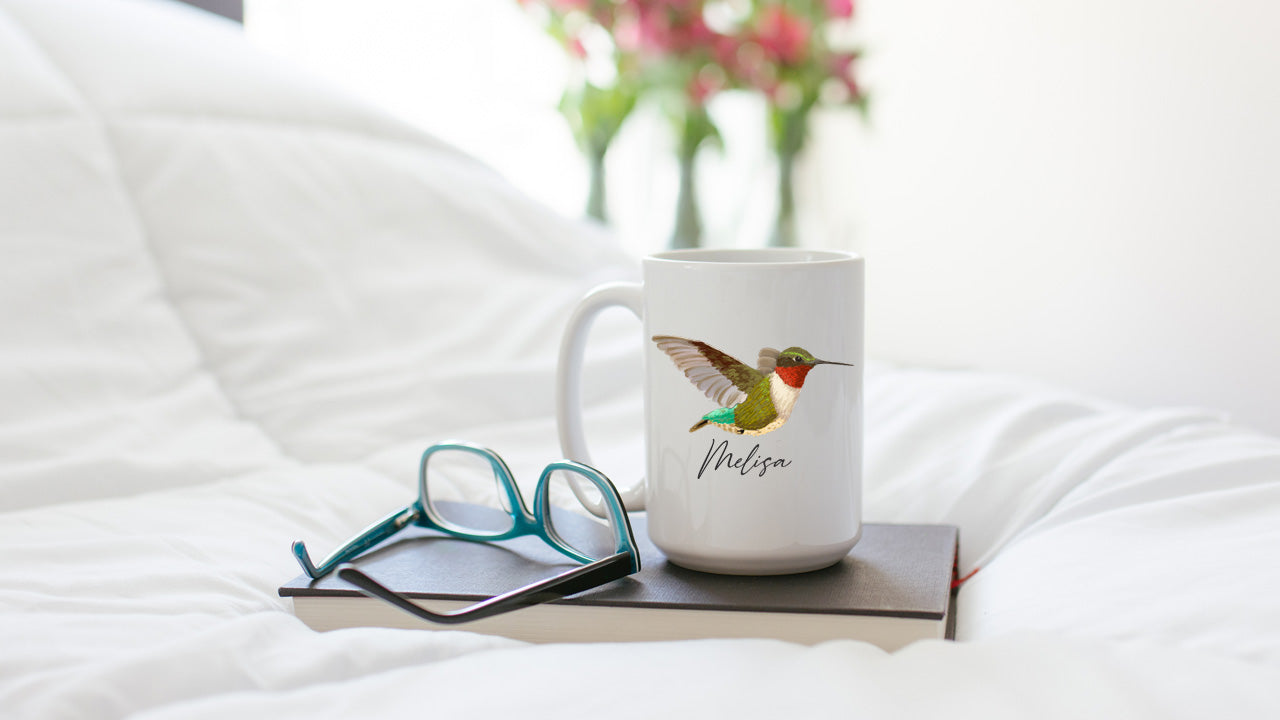 Hummingbird mug sitting on book with glasses on comforter