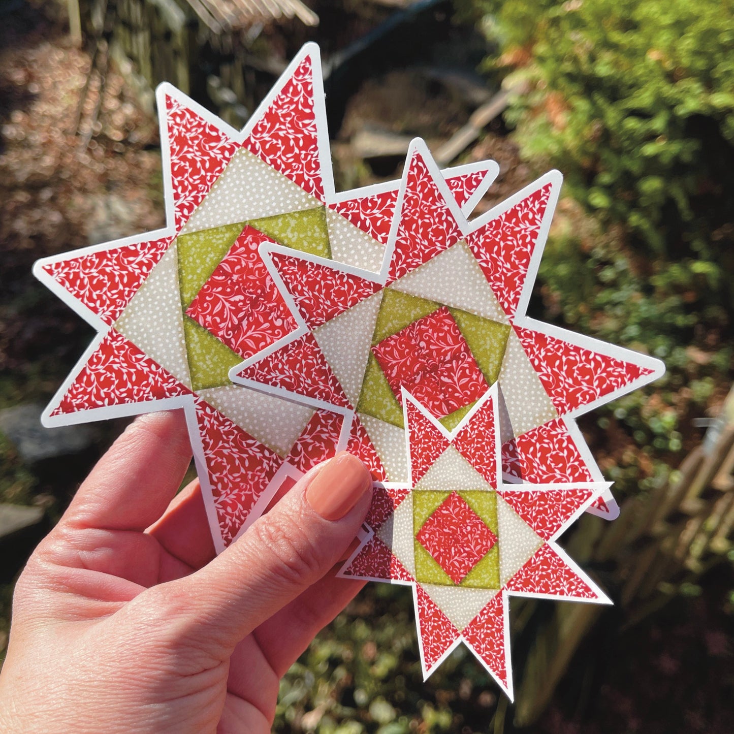 Red, Green and Tan Quilt block stickers in three sizes held over grassy outside background.
