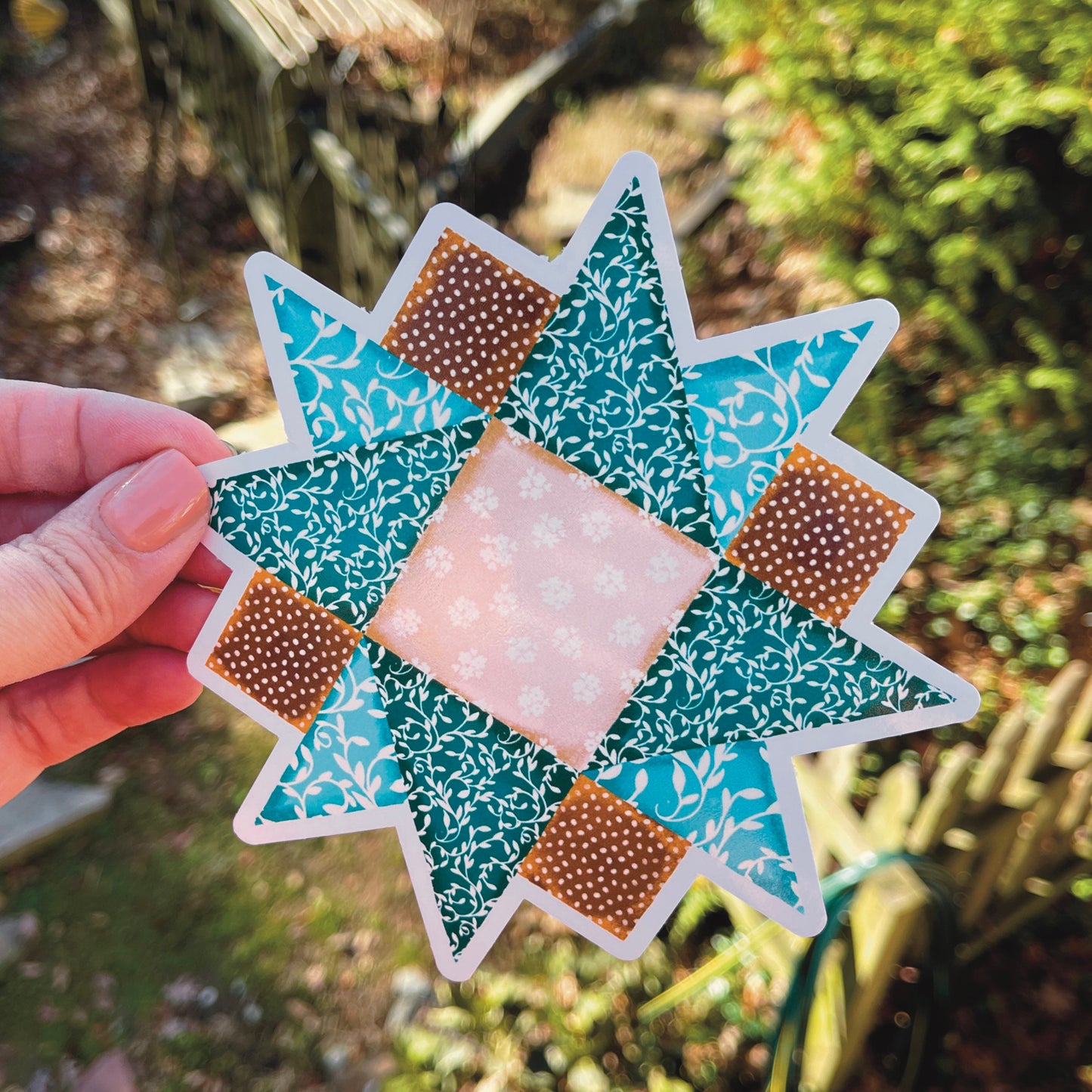 Large brown and blue quilt block sticker held against outdoor background.