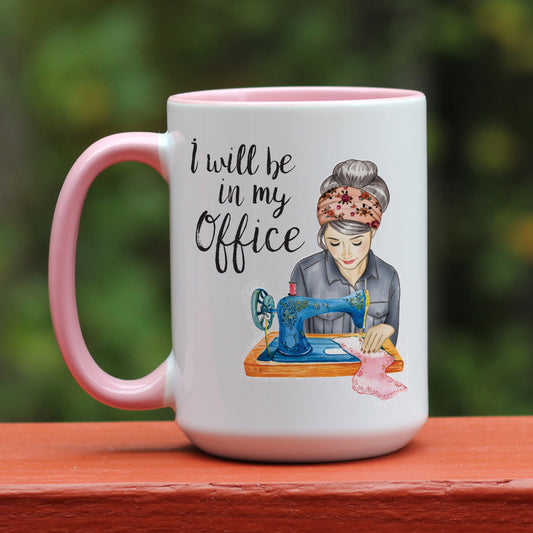 I will be my office sewing coffee mug featuring a woman with gray hair, light skin and antique sewing machine on a white mug with pink handle.