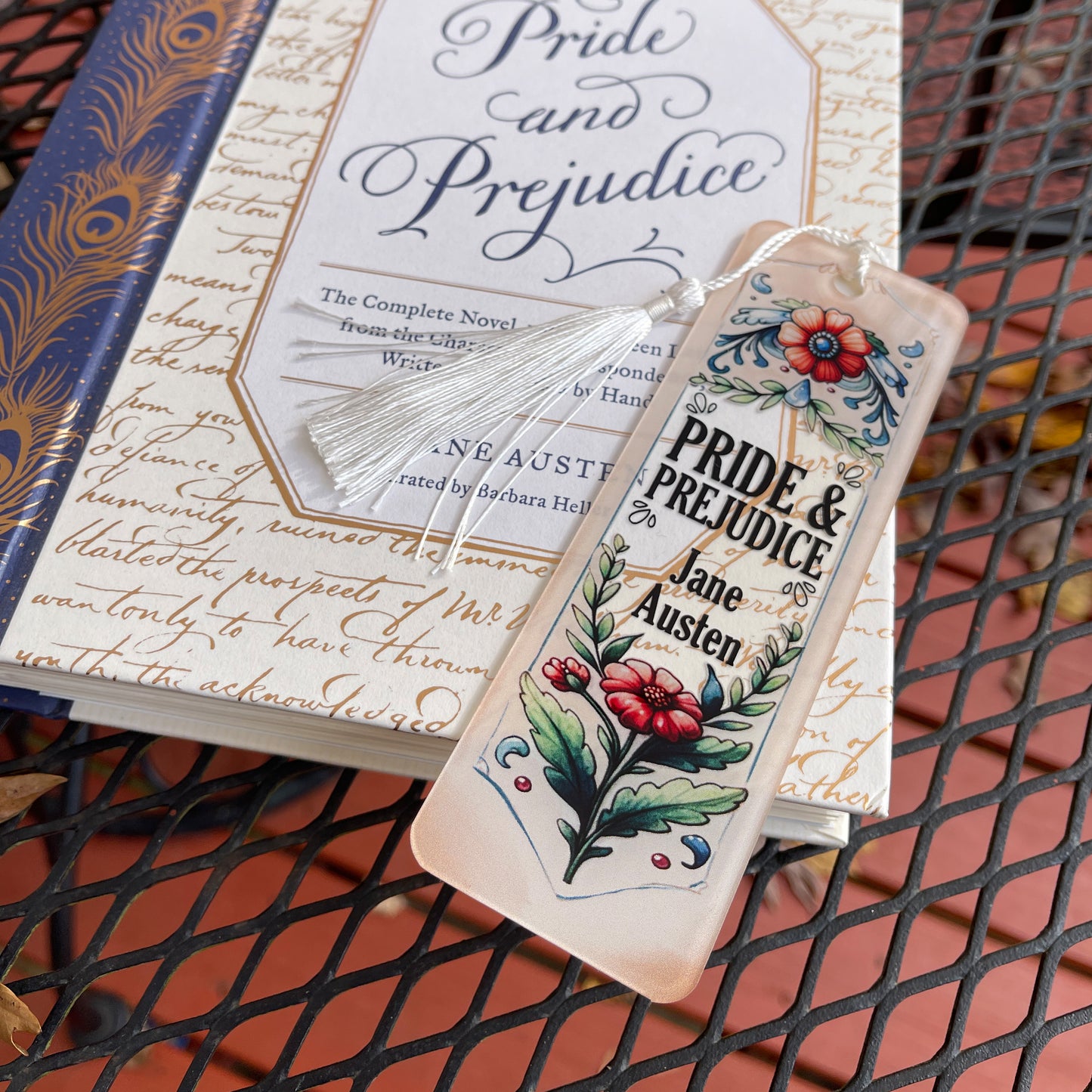 Jane Austen Pride and Prejudice floral acrylic bookmark with tassel laying on closed Pride and Prejudice book.