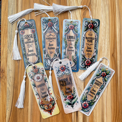 Seven Jane Austen floral acrylic bookmarks representing all her books with tassels arranged on wood background.