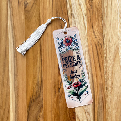 Jane Austen Pride and Prejudice floral acrylic bookmark with tassel laying on wood background.