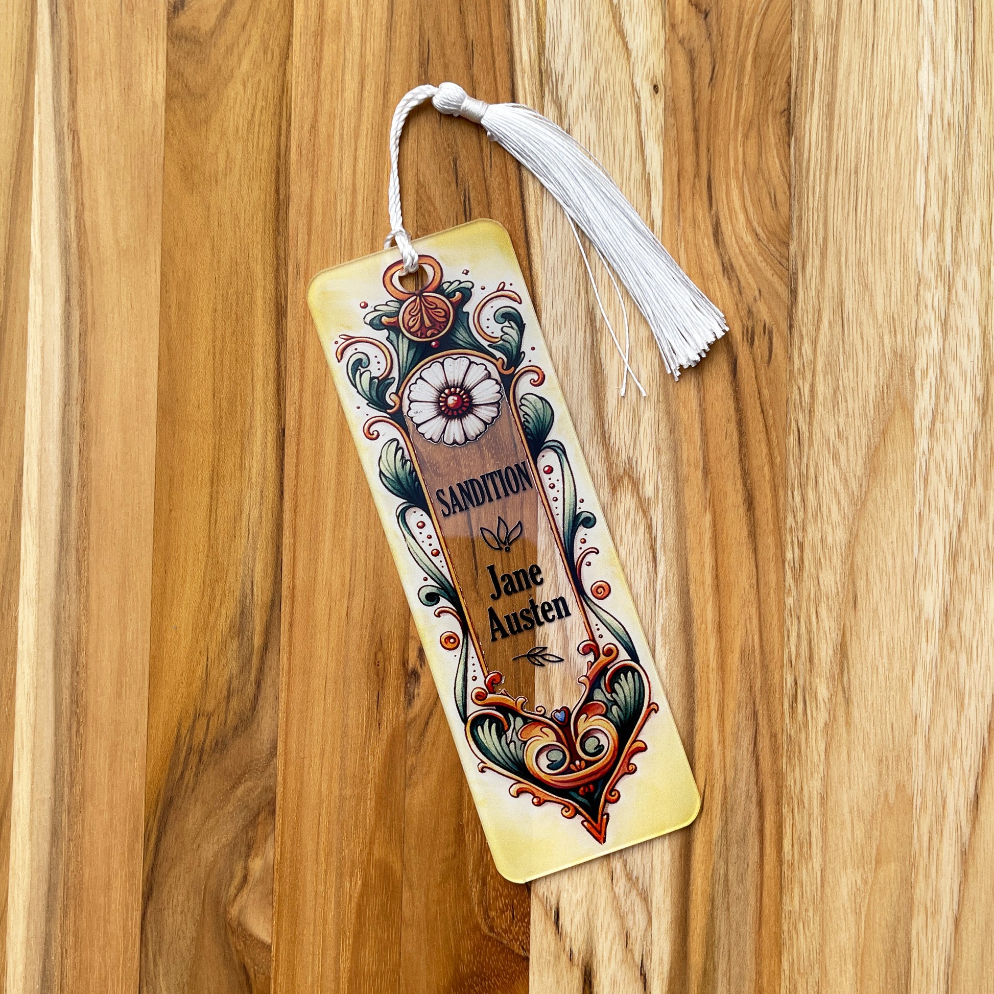 Jane Austen Sandition floral acrylic bookmark with tassel laying on wood background.