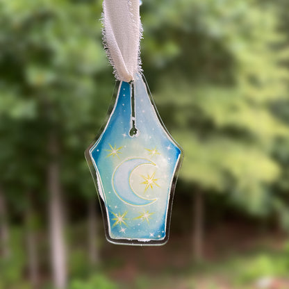 Acrylic fountain pen nib design ornament featuring moon and stars hanging against blurred background.