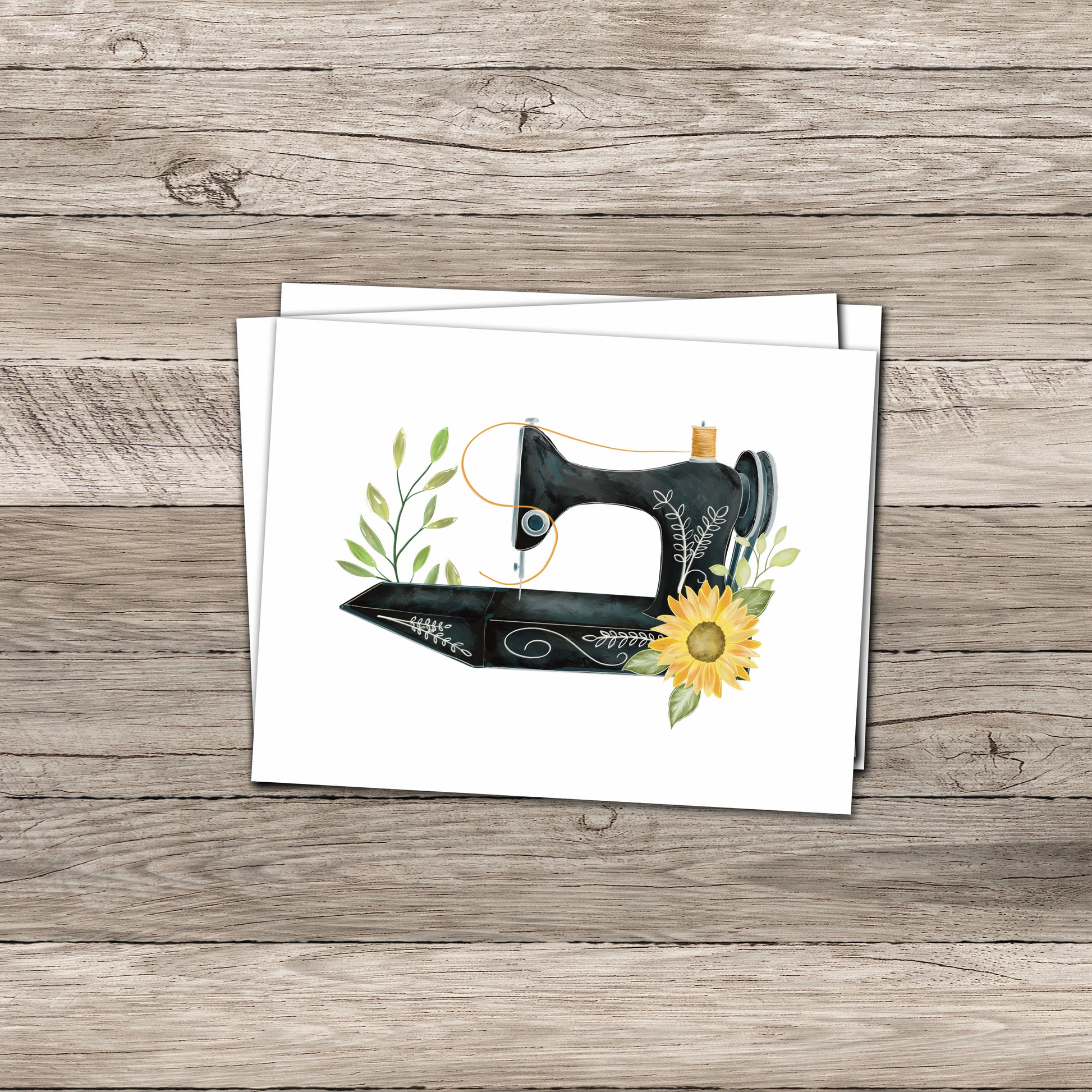 A greeting card featuring an illustration of a vintage black sewing machine adorned with delicate greenery and a bright yellow sunflower displayed on a light wooden surface, accompanied by a plain white envelope.