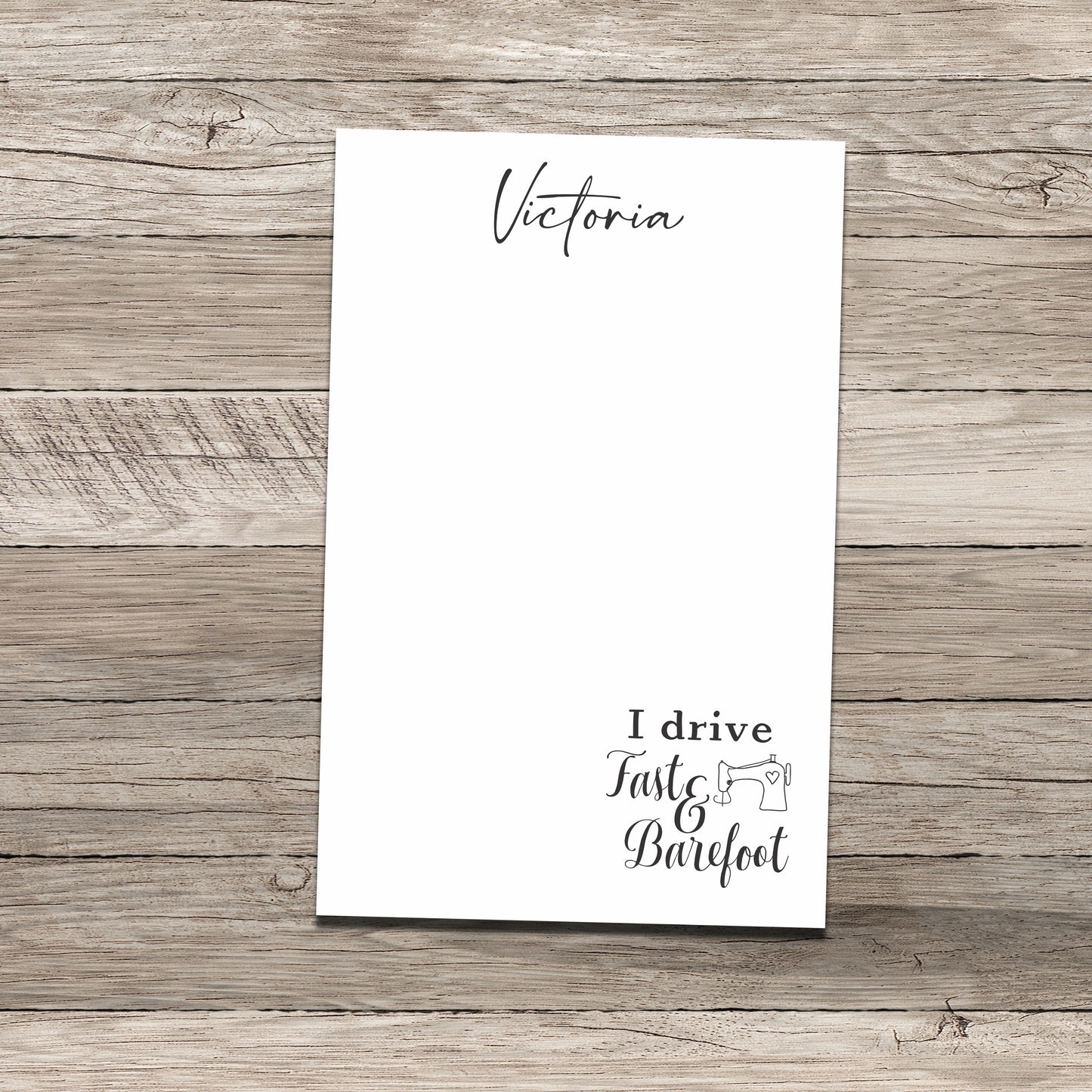 Personalized notepad set featuring the name 'Victoria' at the top and a sewing-themed phrase at the bottom that reads 'I drive Fast & Barefoot' with a sewing machine illustration, printed on a white background with a wood-textured backdrop.