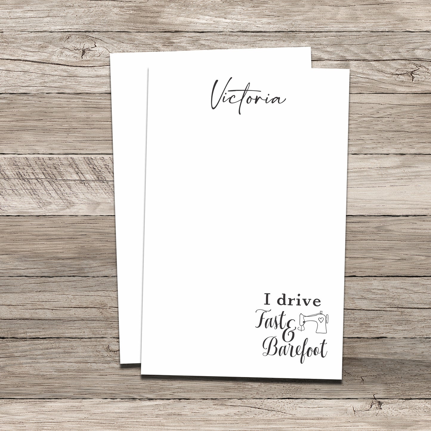 Personalized notepad set featuring the name 'Victoria' at the top and a sewing-themed phrase at the bottom that reads 'I drive Fast & Barefoot' with a sewing machine illustration, printed on a white background with a wood-textured backdrop.