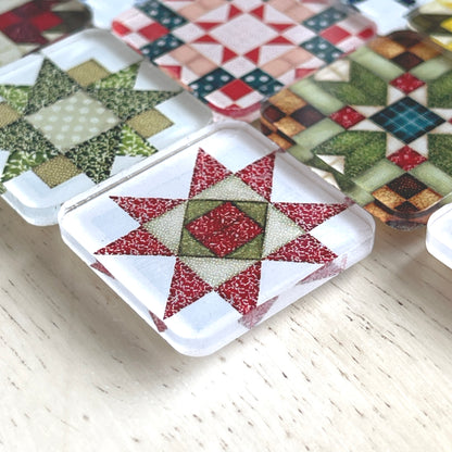 Up close view square magnets featuring various quilt block designs in different colors, including red, green, blue, and yellow. The magnets are arranged on a light wooden surface, each showcasing a unique patchwork pattern.