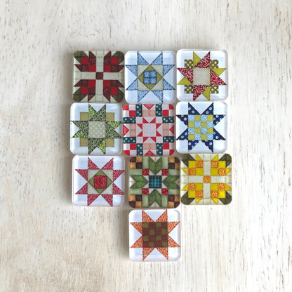 Set of ten square magnets featuring various quilt block designs in different colors, including red, green, blue, and yellow. The magnets are arranged on a light wooden surface, each showcasing a unique patchwork pattern.