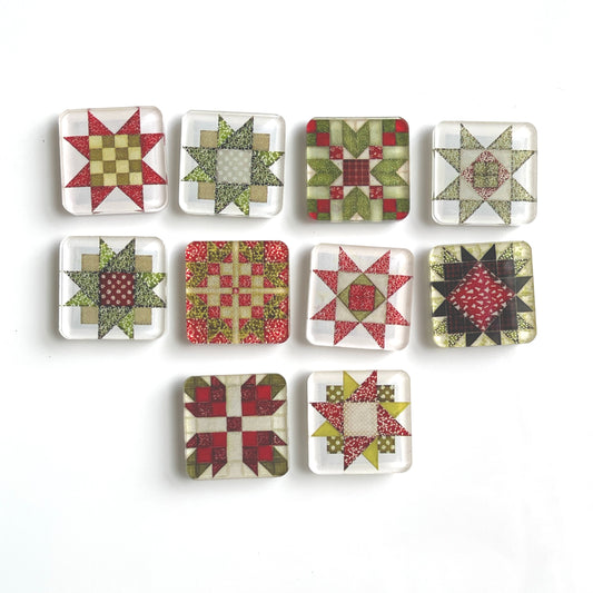 Set of ten square magnets featuring colorful Christmas-themed quilt block designs in traditional red, green, and white patterns. Each magnet showcases a unique quilt patchwork design, arranged in a neat grid on a white background.