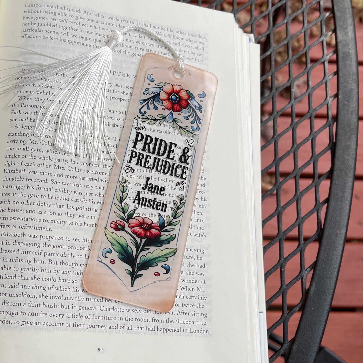 Jane Austen Pride and Prejudice floral acrylic bookmark with tassel laying on page of open book.