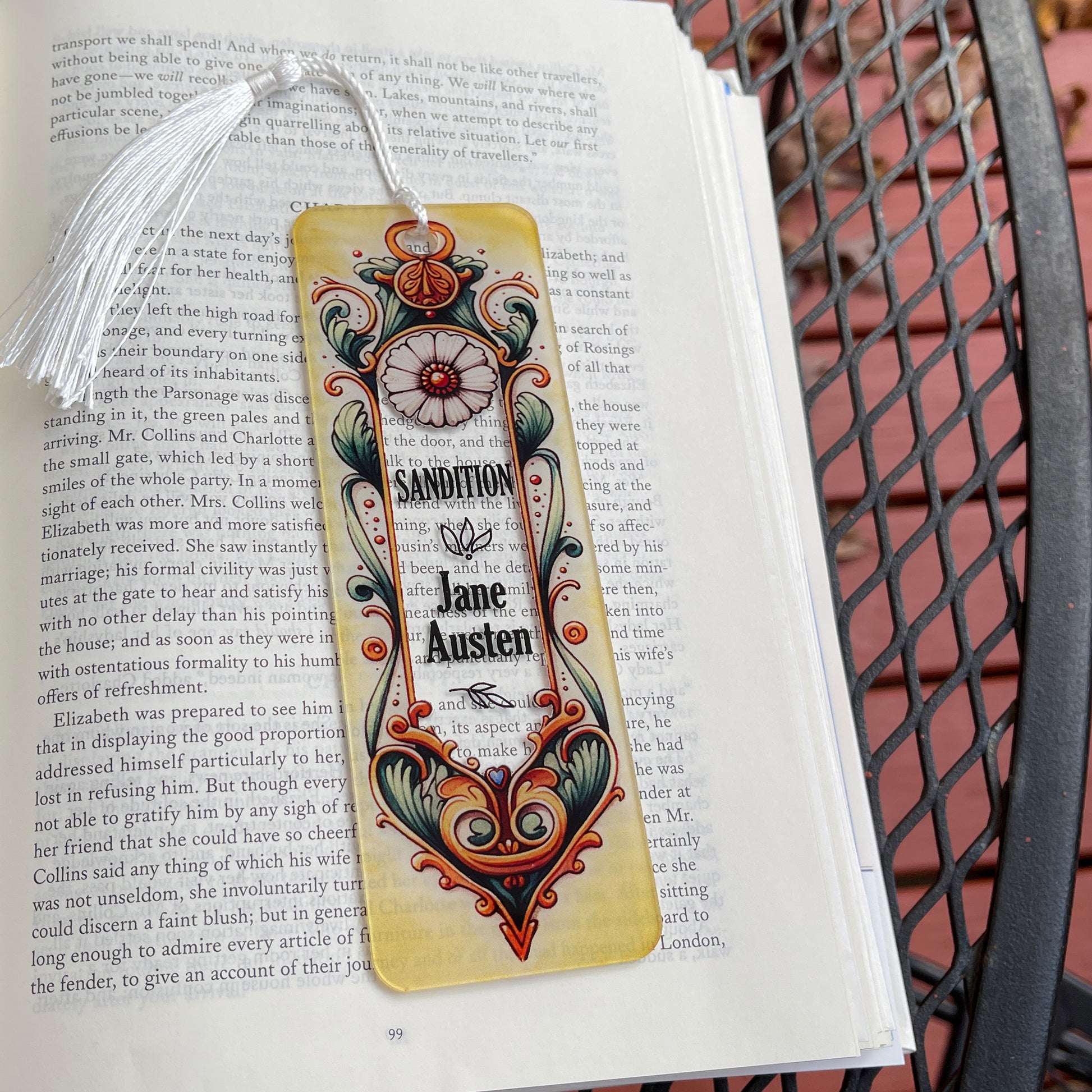 Jane Austen Sandition floral acrylic bookmark with tassel laying on page of open book.