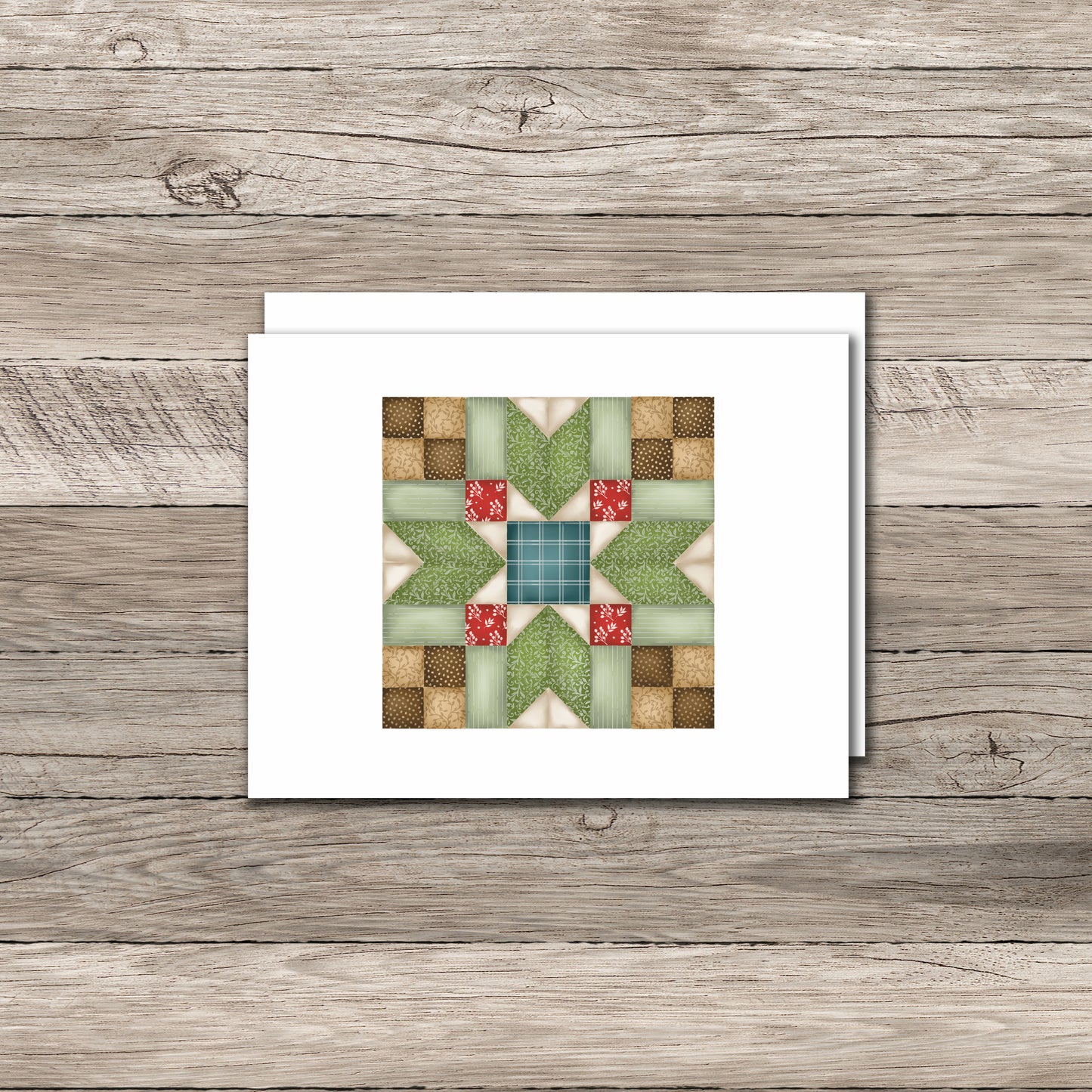 Handmade greeting card with a quilt pattern design featuring green, red, and beige fabric squares arranged in a star-like pattern, placed on a light wood surface with a white envelope beside it.