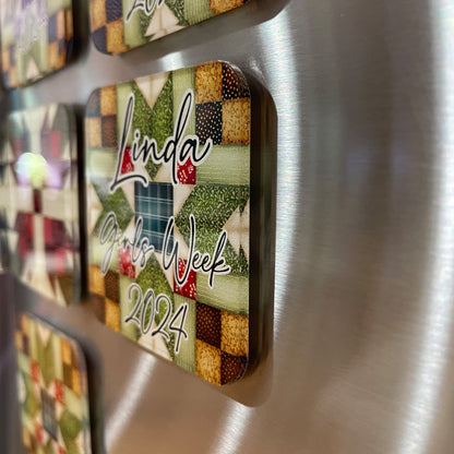 Side view of several square magnets with quilt patterns attached to a metallic surface. The front magnet features a design with green, red, and beige colors and is personalized with the text 'Linda Girls Week 2024.