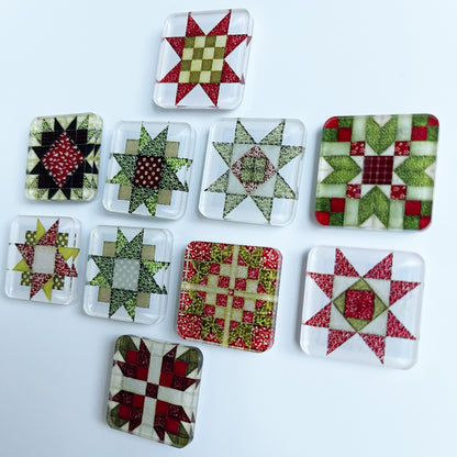 Set of ten square magnets featuring colorful Christmas-themed quilt block designs in traditional red, green, and white patterns. Each magnet showcases a unique quilt patchwork design, arranged in a neat grid on a white background.