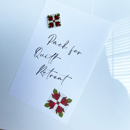 Christmas-themed quilt block magnet holding a note on a white board. The magnet features a red floral quilt patchwork design, securing a handwritten note that reads 'Pack for Quilt Retreat' in elegant script.