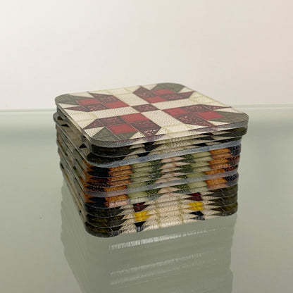 A stack of square magnets with various quilt pattern designs neatly piled on a reflective surface. The top magnet features a red, white, and dark green quilt pattern, while the edges of the stack reveal multiple colorful quilt designs.