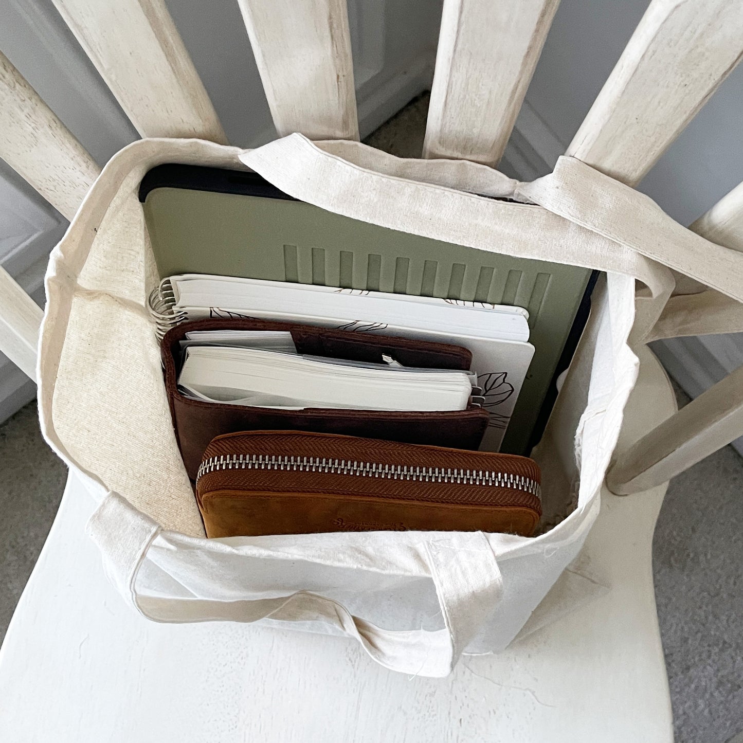 Natural canvas tote bag hanging on a wooden chair, featuring a decorative design of a fountain pen nib with sunflower and leaf motifs, and a delicate laurel wreath below.