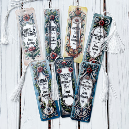 Seven Jane Austen floral acrylic bookmarks representing all her books with tassels arranged on rustic white wood background.