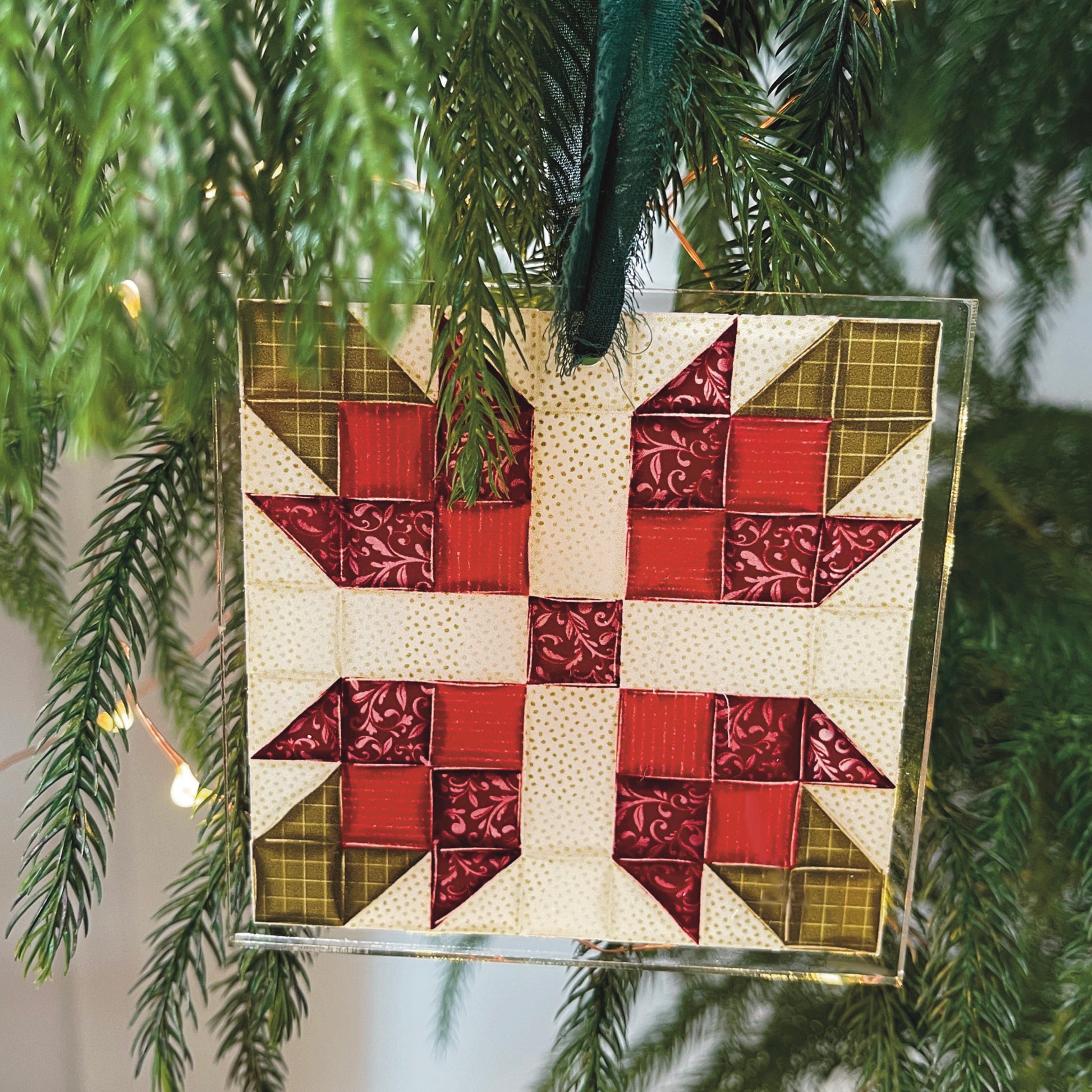 Quilt block ornament with red flower hanging on tree and lights