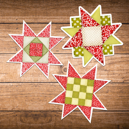 Set of three red and green quilt block stickers laying on dark wood.