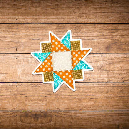 Small orange, blue and brown quilt block sticker laying on dark brown wood.