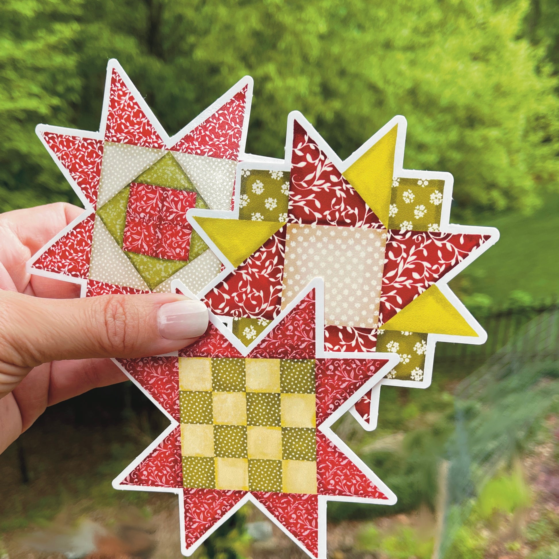 Three versions of medium red and green quilt block sticker held over grassy background.