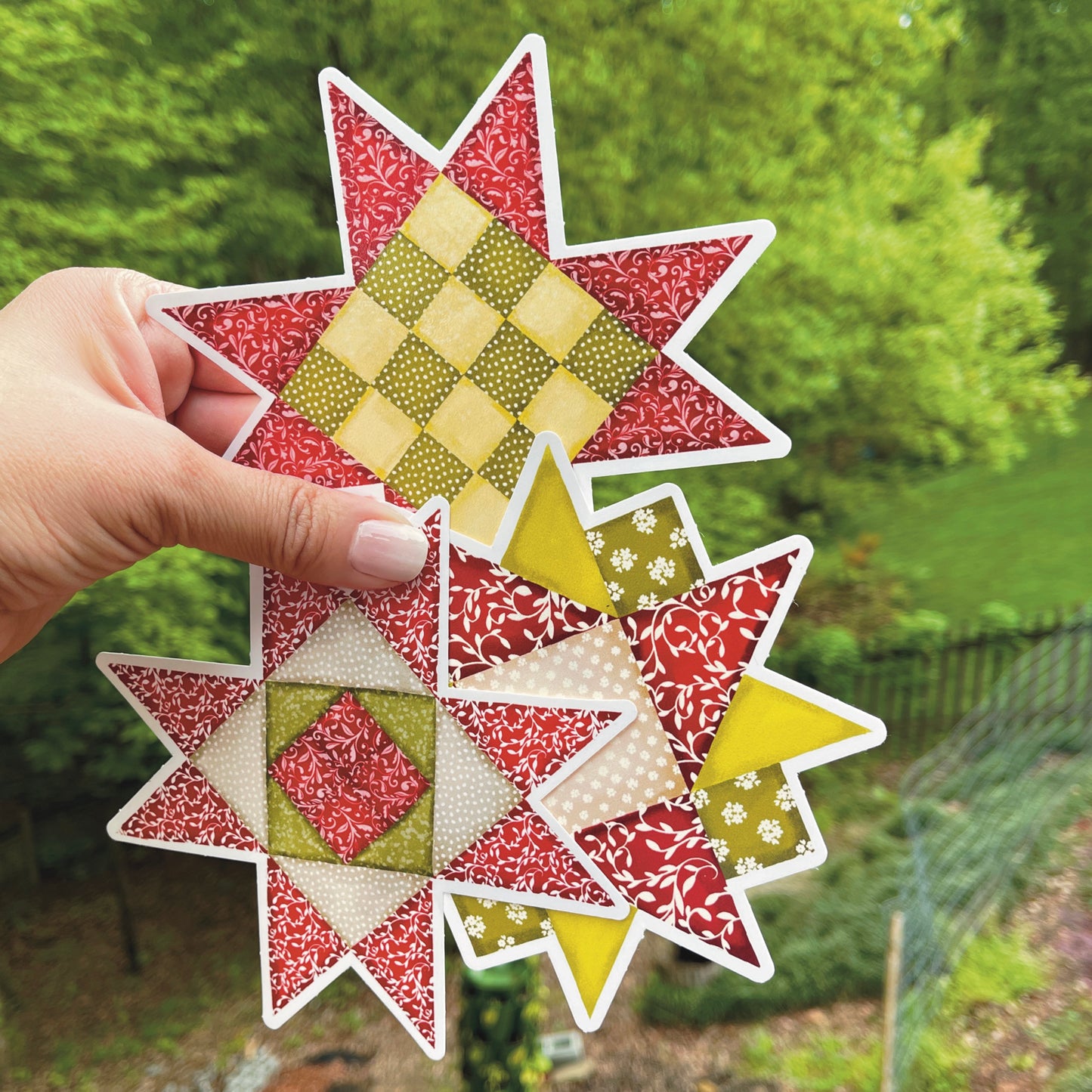 Three versions of large red and green quilt block sticker held over grassy background.